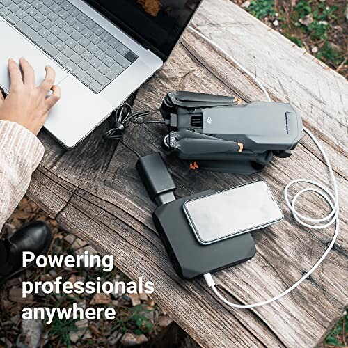 Person using laptop outdoors with portable charger and drone.