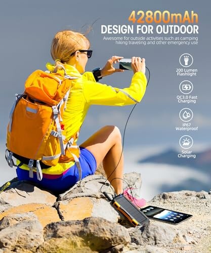 Person using a solar power bank on a mountain with a backpack.